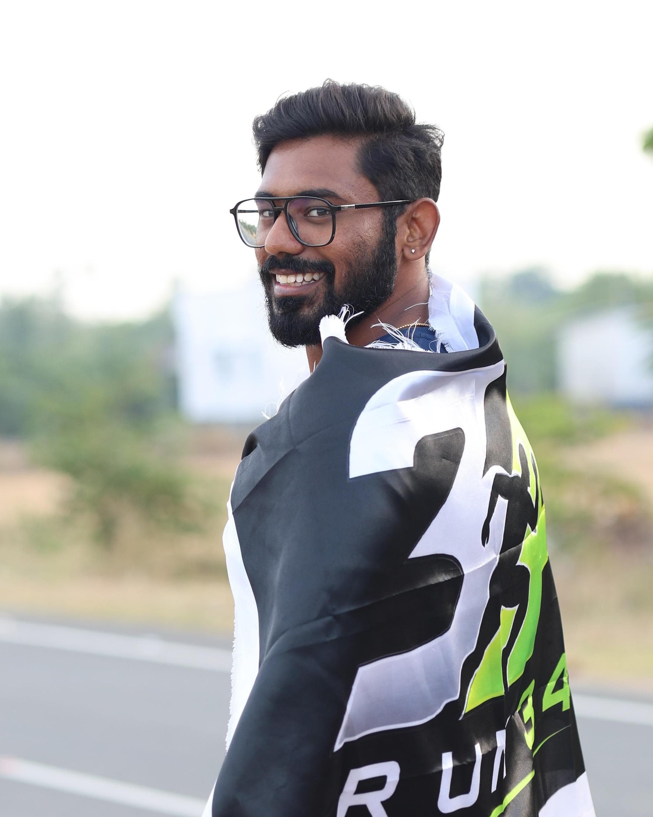 Dharma Surya on the road with a RUN 34 flag around his shoulders, looking back over his shoulder and smiling at the camera.